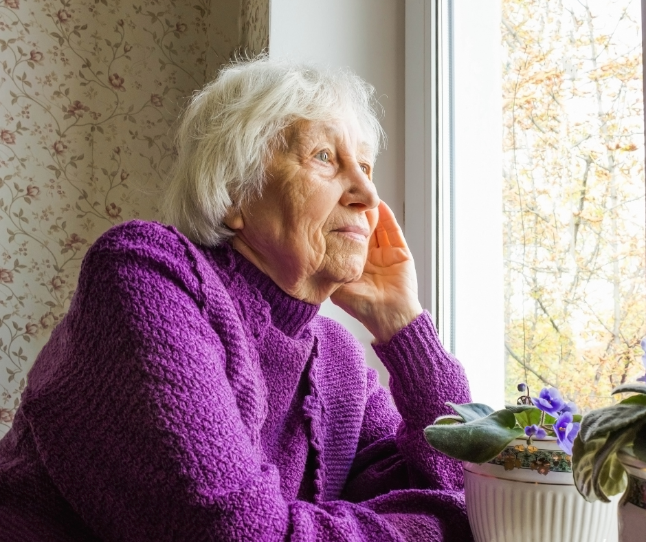 Older lady sat indoors looking out of a window
