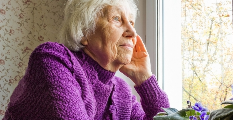Older lady sat indoors looking out of a window