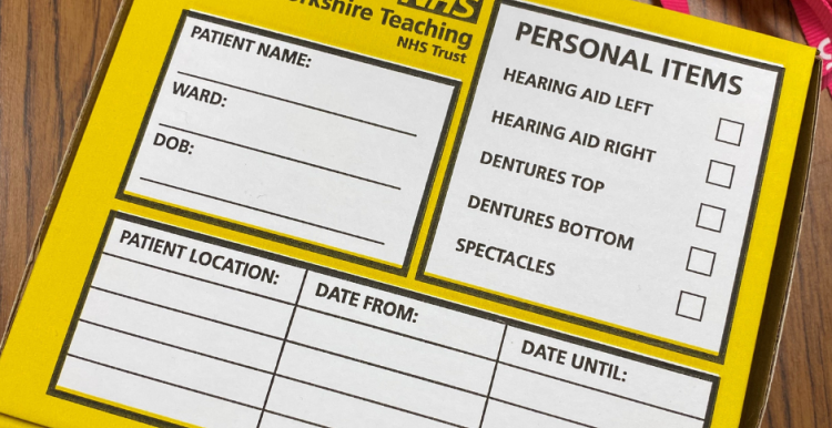A yellow cardboard box with boxes to fill in patient details and to contain their glasses, hearing aids