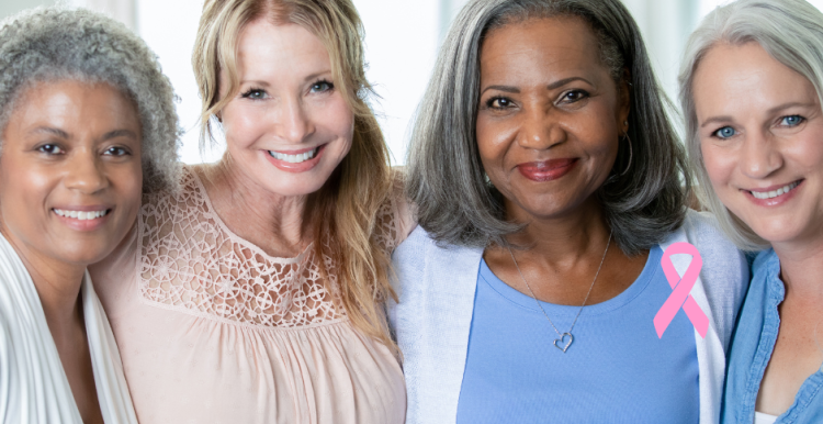 A photo of four middle aged women smiling at the camera with a pink ribbon motif in the bottom right corner