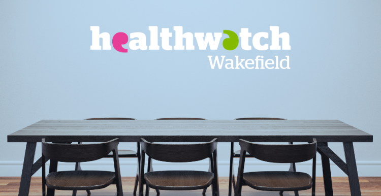 A table and set of chairs with the Healthwatch logo on the wall behind