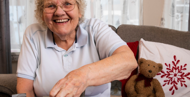 Older lady smiling at the camera playing a jigsaw