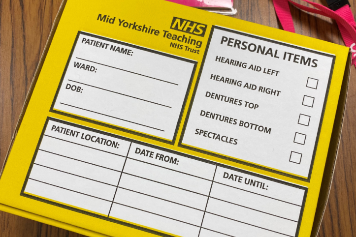 A yellow cardboard box with boxes to fill in patient details and to contain their glasses, hearing aids