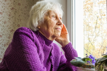 Older lady sat indoors looking out of a window