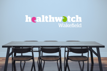 A table and set of chairs with the Healthwatch logo on the wall behind