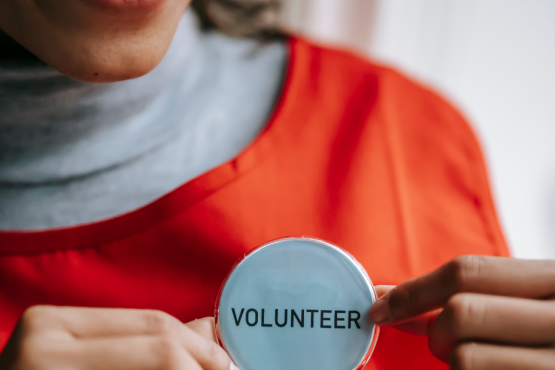 A smiling woman holding a badge that says volunteer