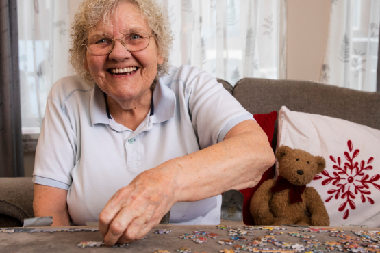 Older lady smiling at the camera playing a jigsaw