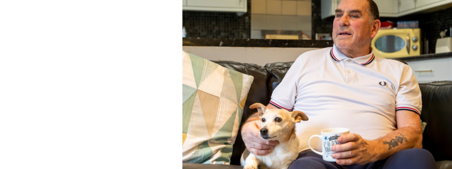 Man sat on a settee looking to the side with his dog