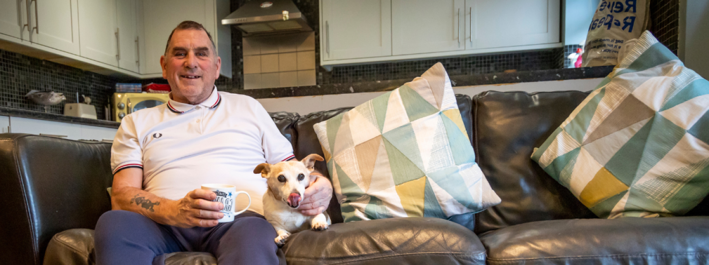 Man sat on sofa smiling at camera with dog